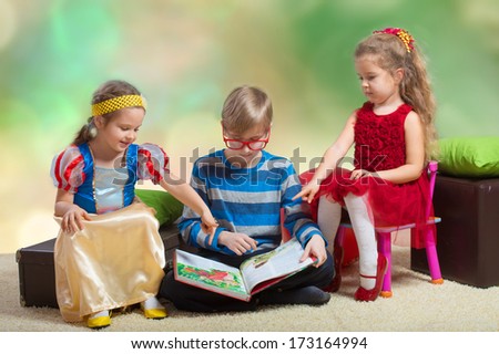 Preteen boy reading a fairy tale to two little girls and showing them the book pictures