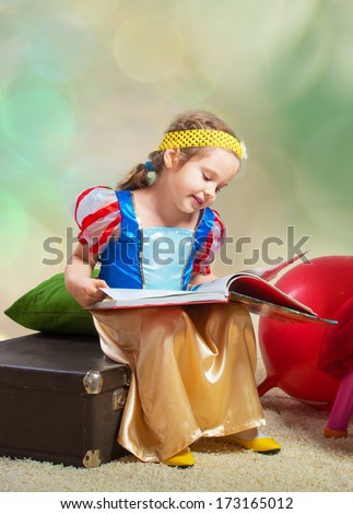 Portrait of a smiling small girl sitting with a book and looking at pictures