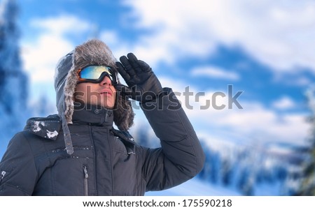 Winter holiday - portrait of a man wearing an ear flap hat and ski glasses with mountains in background