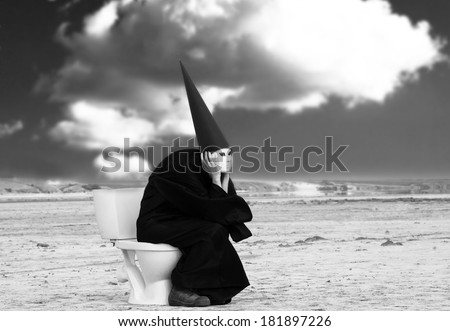Strange person in black cloak sitting on a toilet and thinking in the middle of the desert