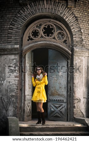 Full-length portrait of a pretty woman in yellow overcoat standing in front of a vintage door