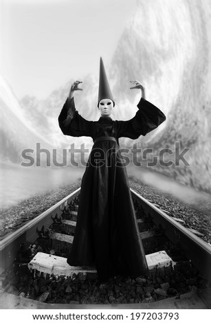 Wizard in black cloak and dunce hat standing on rails. Black and white image