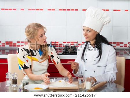 Woman in chef uniform explaining to her younger friend how to make dough