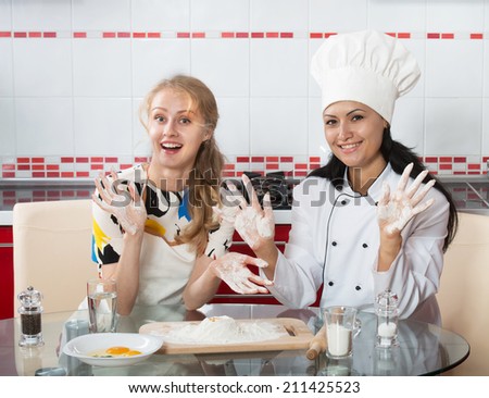 Woman in chef uniform explaining to her younger friend how to make dough