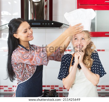 Smiling woman putting a chef hat on her younger friend\'s head
