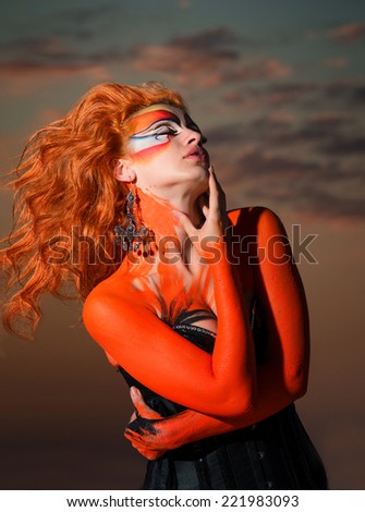 Portrait of a redheaded woman in art make-up and bodyart with sunset in background. Fire spirit.