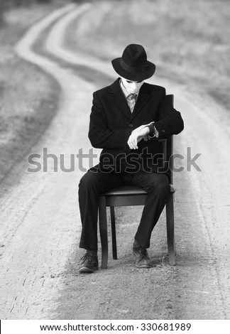 Man in the mask sitting on a chair in the middle of the country road, black and white shot