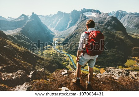 Hiking alone in Norway mountains Man with red backpack enjoying landscape on cliff solo traveling healthy lifestyle concept active summer vacations