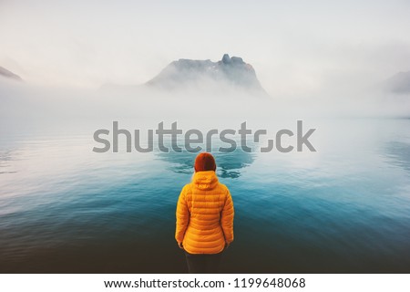 Woman alone looking at foggy sea traveling adventure lifestyle outdoor solitude sad emotions winter down jacket clothing cold scandinavian minimal landscape
