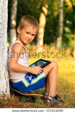 Boy Child playing with Tablet PC sitting on skateboard Outdoor with forest on background Game Dependence concept
