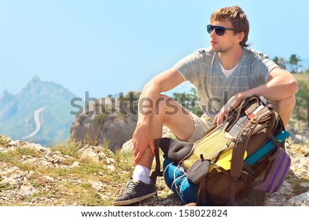 Young Man Traveler with backpack relaxing on Mountain summit rocky cliff  with aerial view of Sea on background Hiking and Healthy Lifestyle concept