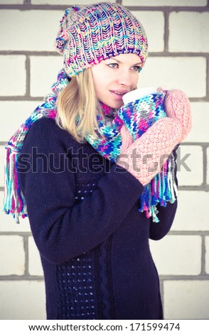 Young Woman heating with coffee cup Winter time wearing knitted sweater, hat and scarf with mittens Lifestyle concept with white brick wall on background