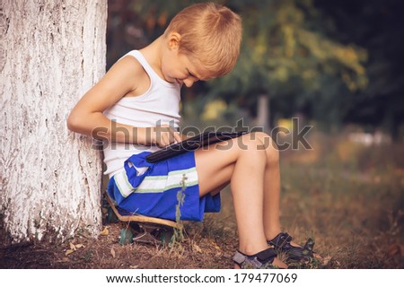 Boy Child playing with Tablet PC Outdoor with Summer nature on background Computer Game Dependence concept Lifestyle