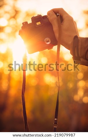 Man hand holding retro photo camera outdoor hipster Lifestyle with sun lights bokeh autumn nature on background