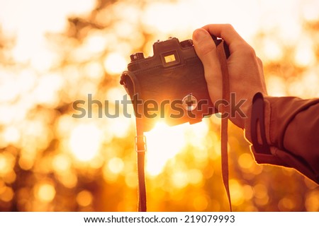 Man hand holding retro photo camera outdoor hipster Lifestyle with sun lights bokeh autumn nature on background