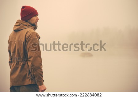 Young Man standing alone outdoor with foggy scandinavian nature on background Travel Lifestyle and melancholy emotions concept film effects colors