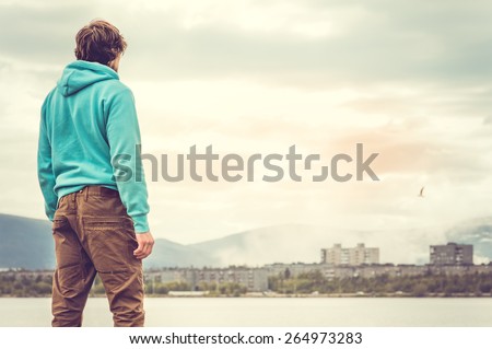 Young Man standing alone outdoor Travel Lifestyle concept with lake and city on background