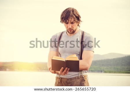 Young Man reading book outdoor with scandinavian lake on background Education and Lifestyle Travel concept
