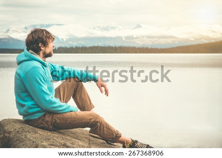Young Man relaxing alone outdoor Lifestyle Travel concept scandinavian mountains and lake on background