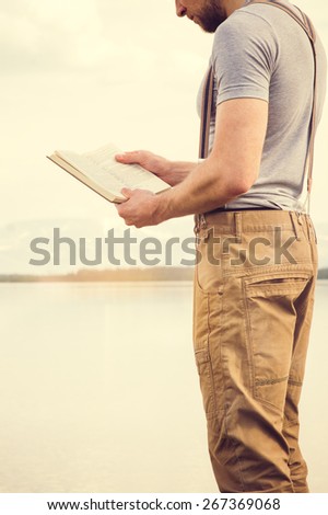 Young Man reading book outdoor with scandinavian lake and mountains on background Education and Lifestyle Travel concept