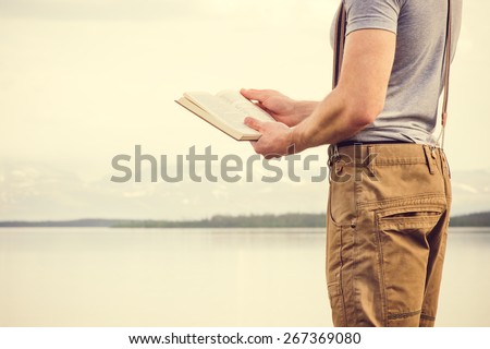 Young Man reading book outdoor with scandinavian lake and mountains on background Education and Lifestyle Travel concept