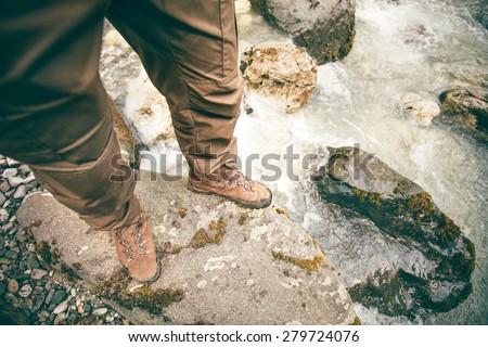 Feet Man trekking boots hiking outdoor Lifestyle Travel survival concept with river and stones on background top view