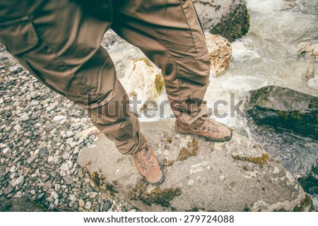 Feet Man trekking boots hiking outdoor Lifestyle Travel survival concept with river and stones on background top view