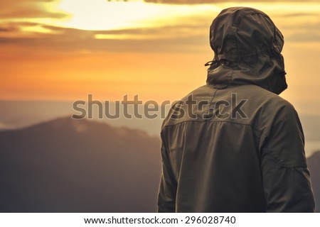 Young Man standing alone outdoor with sunset mountains on background Travel Lifestyle and survival concept rear view