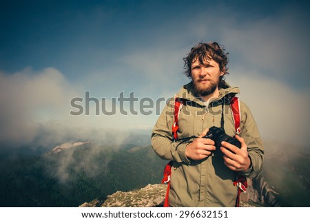 Man Traveler with photo camera and backpack hiking outdoor Travel Lifestyle survival concept with mountains clouds on background