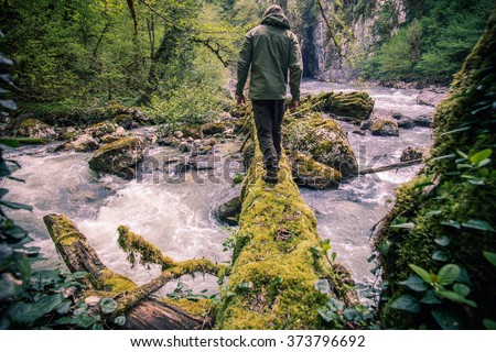 Man Traveler crossing river on log outdoor Lifestyle Travel survival concept
