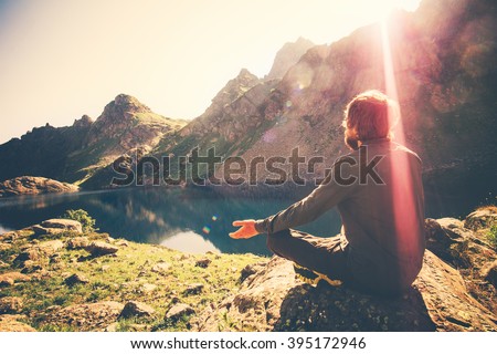 Bearded Man meditating yoga relaxing alone sitting lotus pose on stone Travel healthy Lifestyle concept lake and mountains sunny landscape on background outdoor