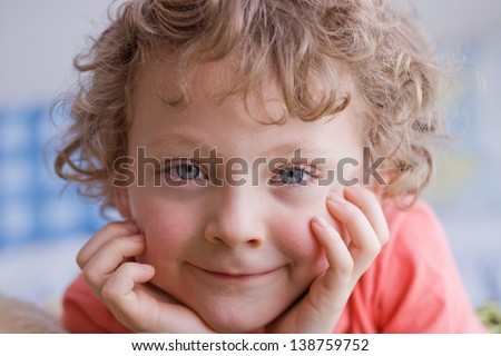 close up portrait of a curly haired boy with his chin resting in his hands