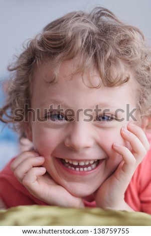 close up portrait of a happy smiling curly haired boy, with his chin resting in his hands