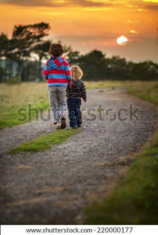 two young brothers walking together down a path towards the setting sun