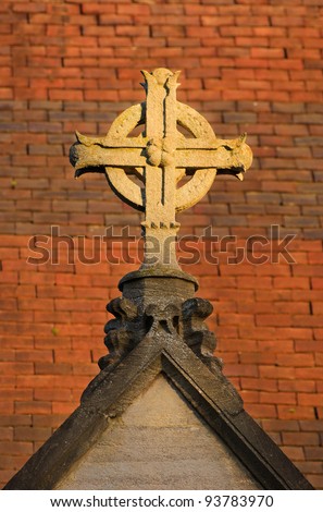Anglican cross on a church roof, with a background of red clay roof tiles, lit by late afternoon sun