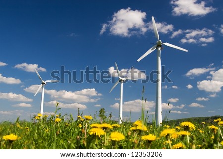 Wind Farm against blue sky with white clouds and yellow flowers on the ground