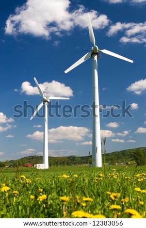Windmills against blue sky with white clouds and yellow flowers on the ground