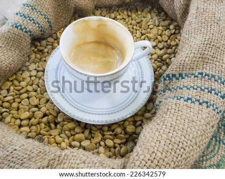 white cup of coffee on raw coffee bean ready to roast