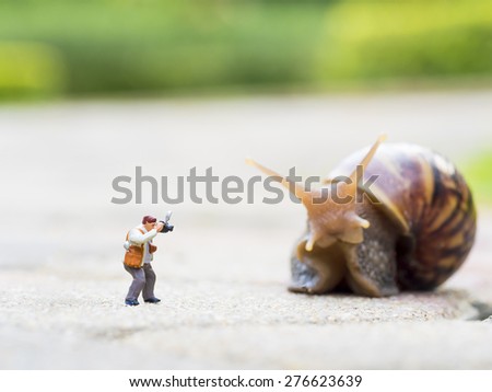 toy charactor in using camera action pointing to big snail in nature outdoor