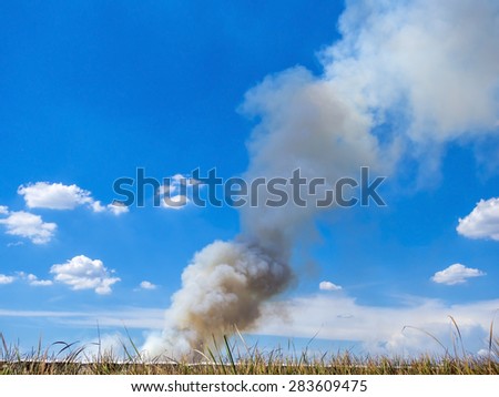 Burning house causes a big pile of smoke, black smoke rising up to blue sky background.