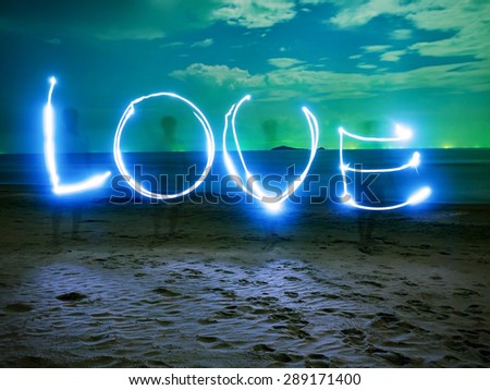 hand writing the word of LOVE, by using flash light, on the night at sea beach