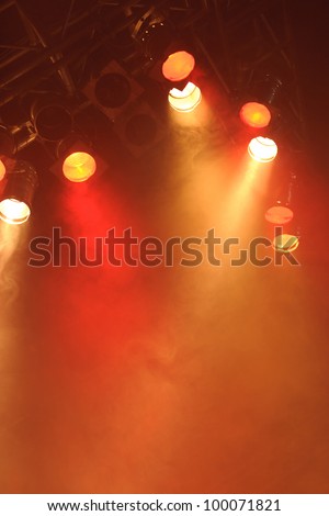 Bright spotlights shining down on to an empty stage creating a deep orange red misty or smokey glow