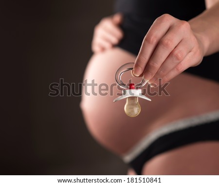 Rubber pacifier close up and pregnant woman