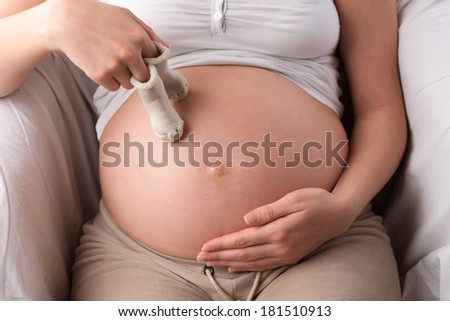 Naked belly closeup of a pregnant woman holding a pair of white baby socks on her tummy