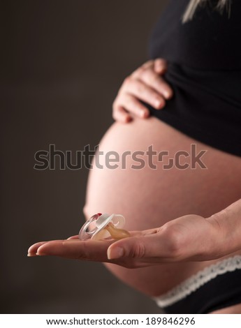 Close-up of a pregnant woman holding baby rubber pacifier in her hand