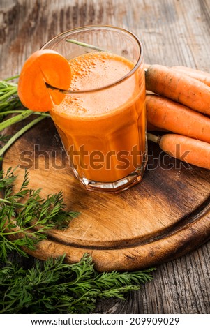 Glasses of carrot juice and fresh carrots on wooden background