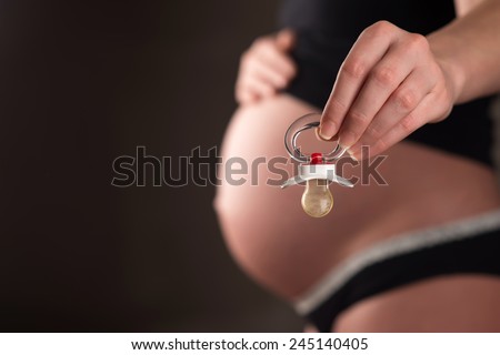 Rubber pacifier close up and pregnant woman