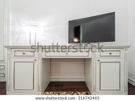 Large black wide screen TV set on the white dresser in a bright room