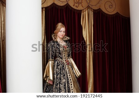 Actress in royal dress posing on curtain backdrop
