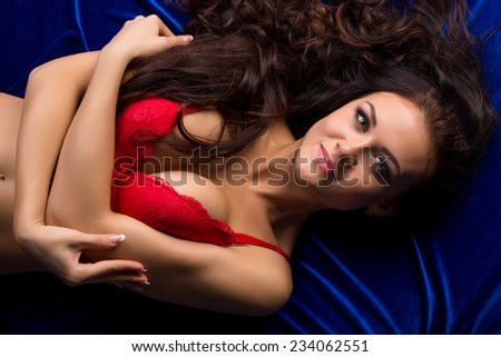 Busty underwear model lying on blue satin sheets